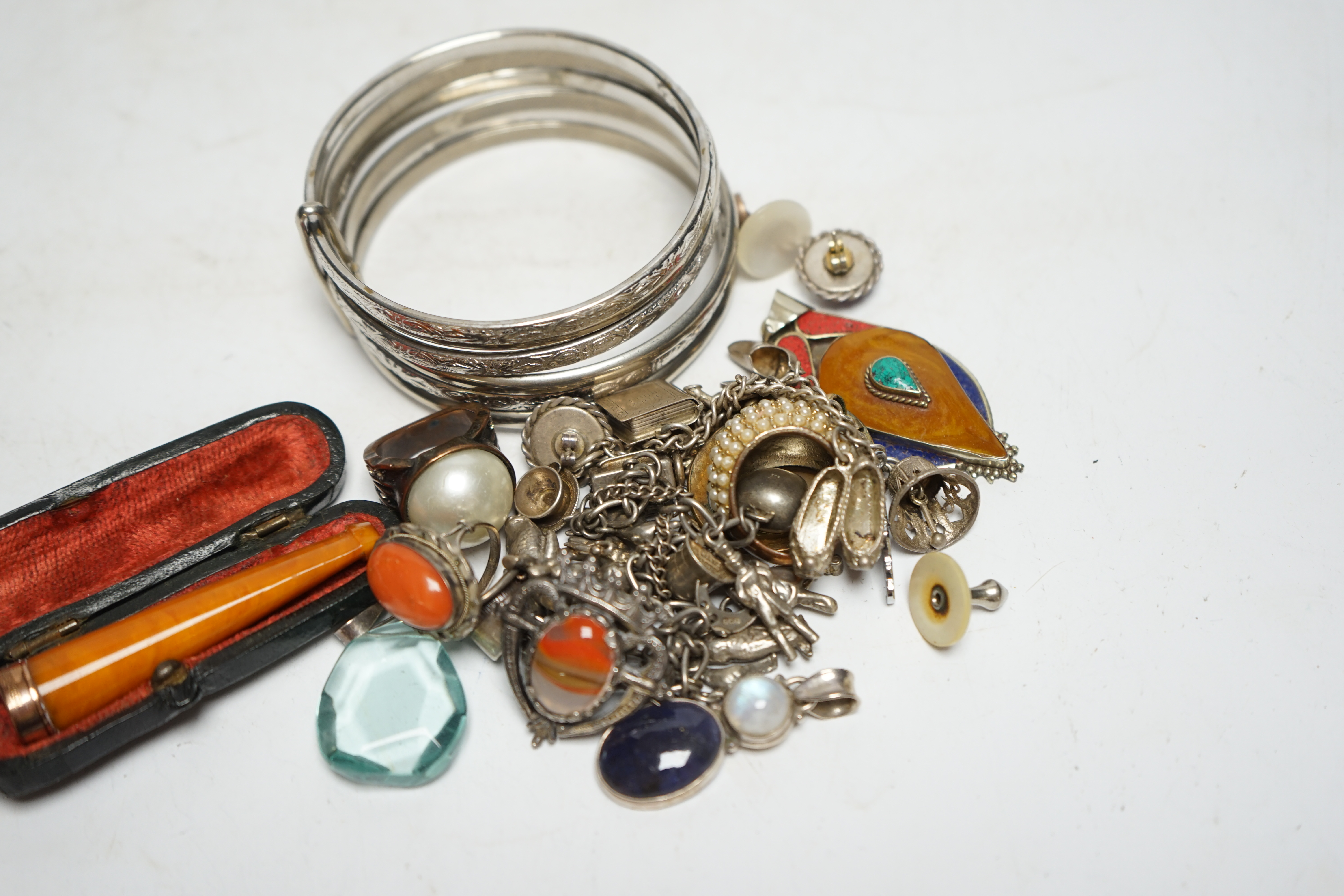 A small group of assorted white metal and costume jewellery including two charm bracelets and a cased 9ct gold mounted amber cigarette holder. Condition - poor to fair